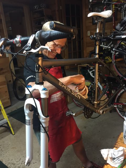 Dennis wearing an apron, using a toothbrush to clean his bike.